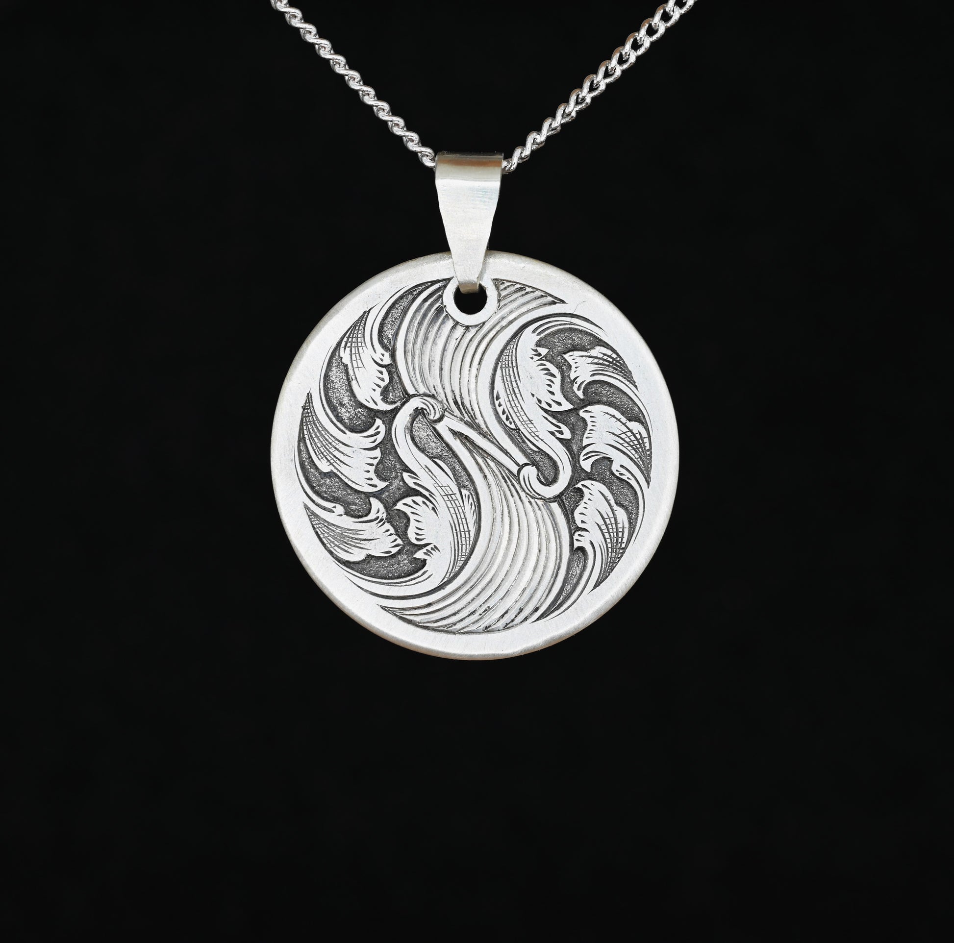 A sterling silver disc pendant with hand-crafted bale featuring an engraved acanthus wave design.