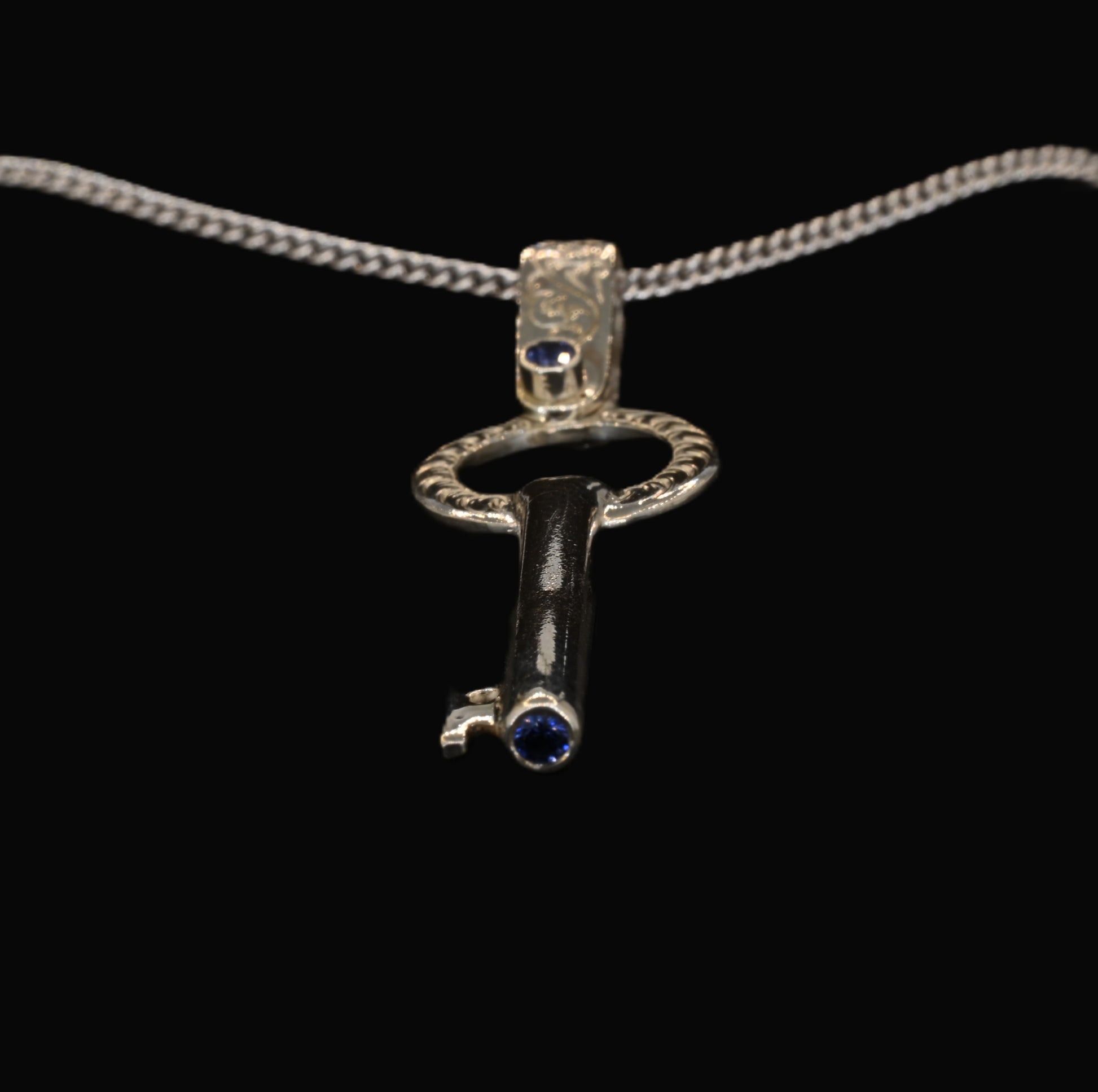 A sterling silver key-shaped pendant with hand-engraved acanthus leaves and ceylon sapphires
