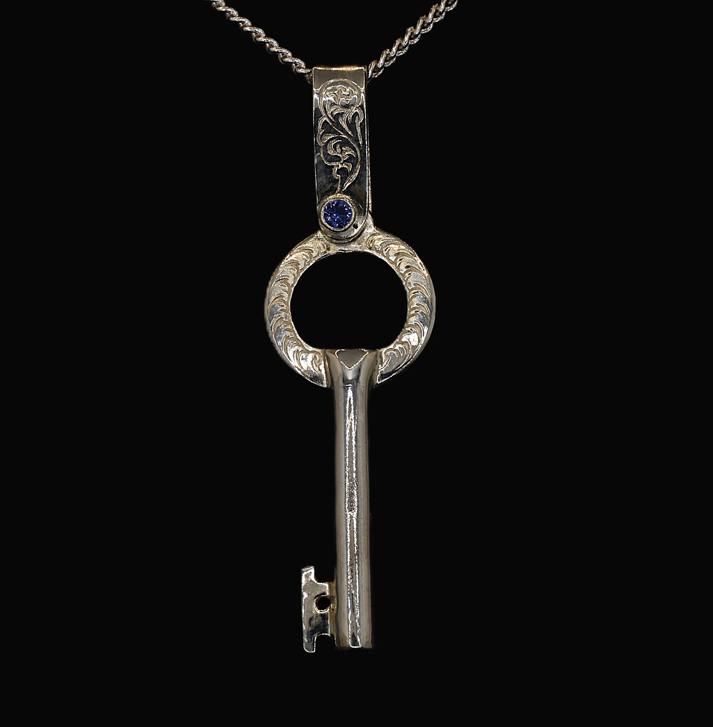 A sterling silver key-shaped pendant with hand-engraved acanthus leaves and ceylon sapphires