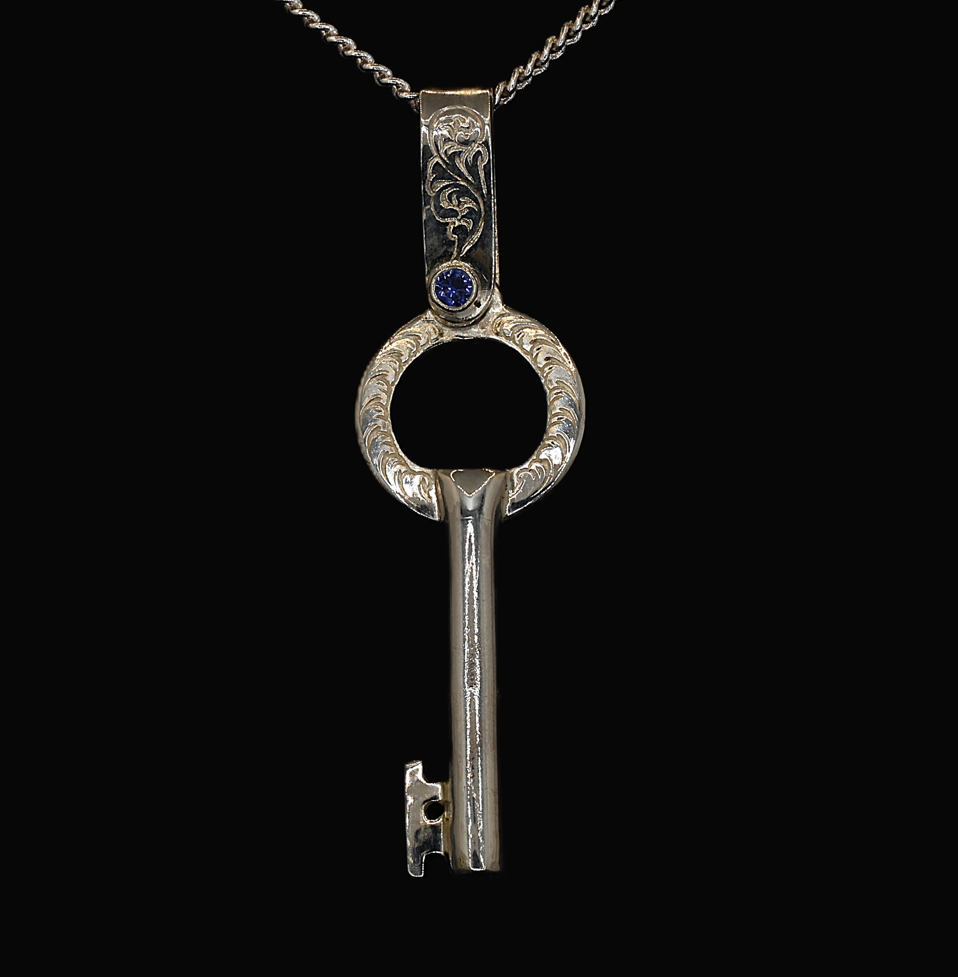 A sterling silver key-shaped pendant with hand-engraved acanthus leaves and ceylon sapphires