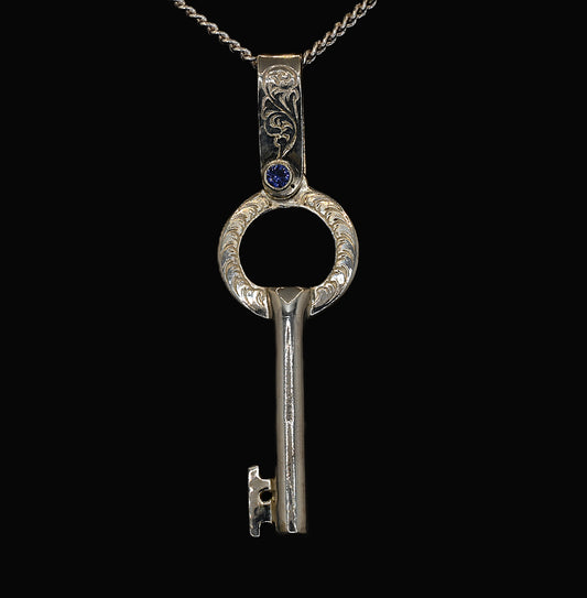 A sterling silver key-shaped pendant with hand-engraved acanthus leaves and ceylon sapphires