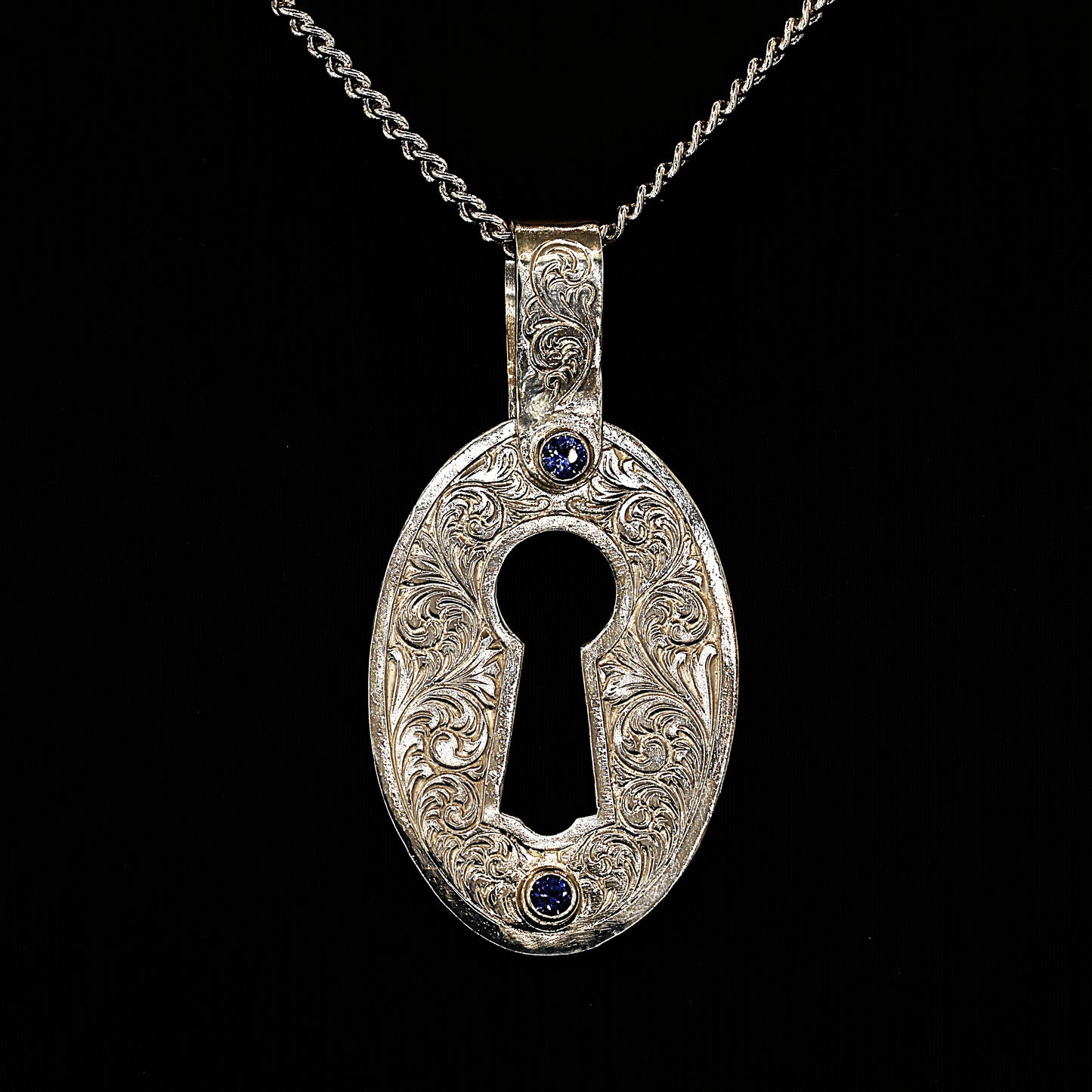A sterling silver pendant with hand-engraved acanthus ceylon sapphires, in the shape of a lock