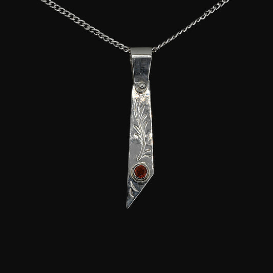 An asymmetric sterling silver pendant with hand-engraving and a bezel-set garnet