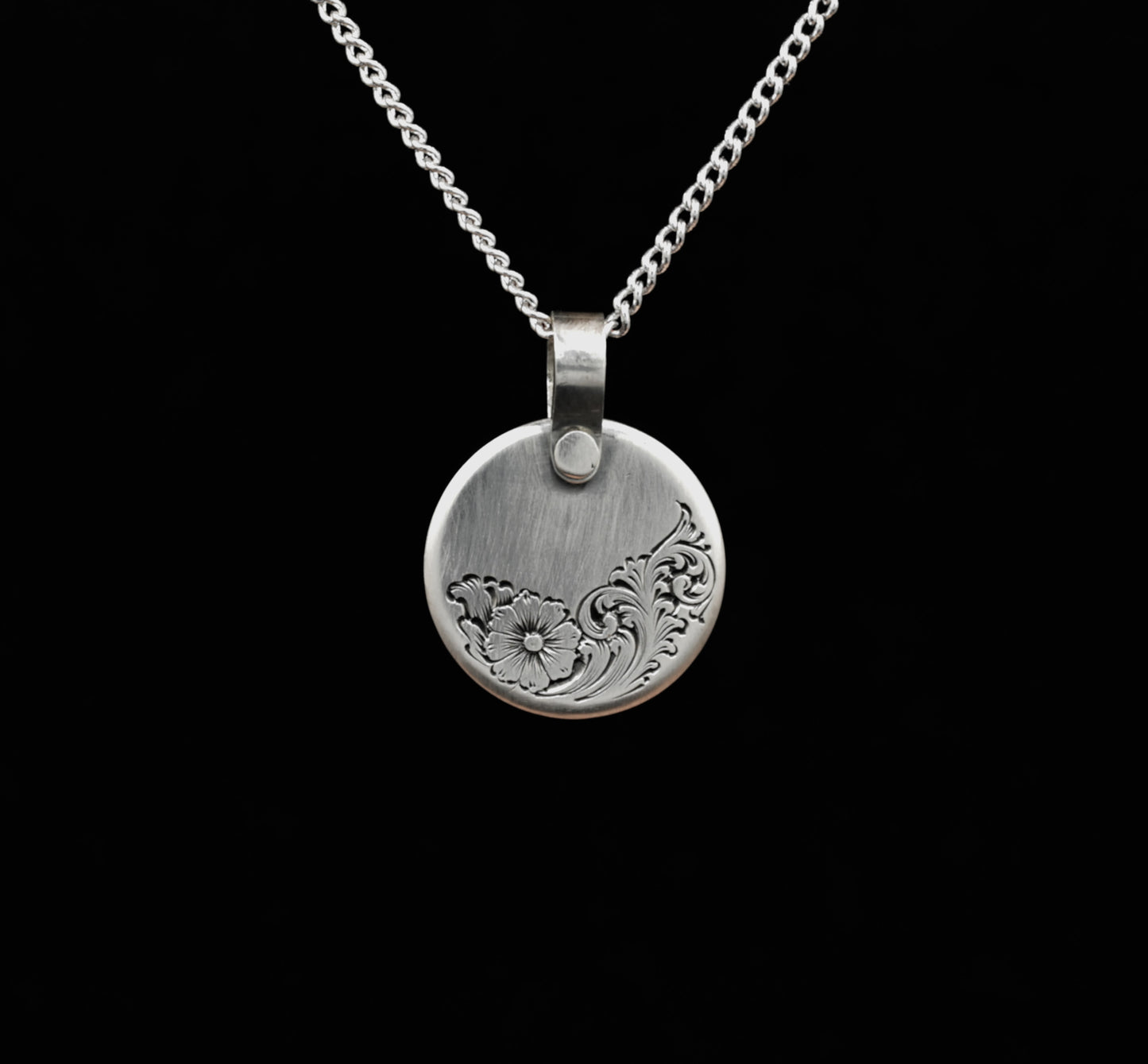 A sterling silver disc pendant with a floral hand-engraving