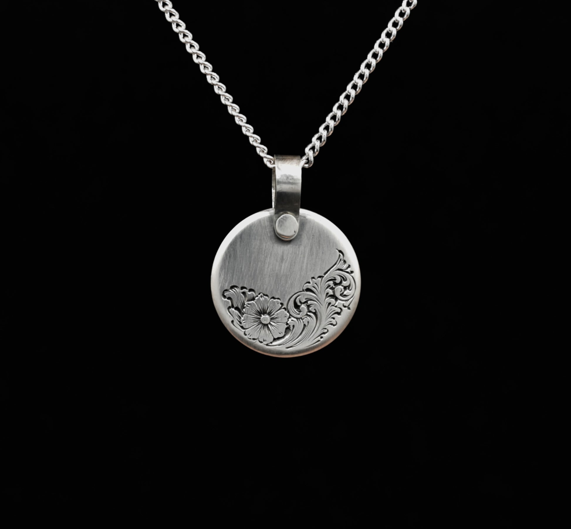 A sterling silver disc pendant with a floral hand-engraving