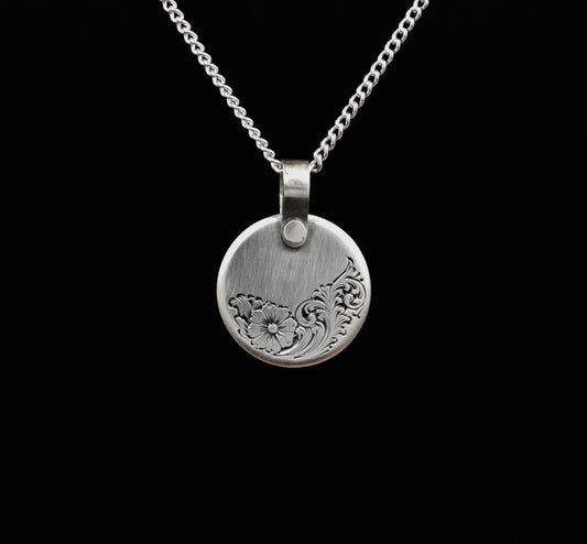 A sterling silver disc pendant with a floral hand-engraving