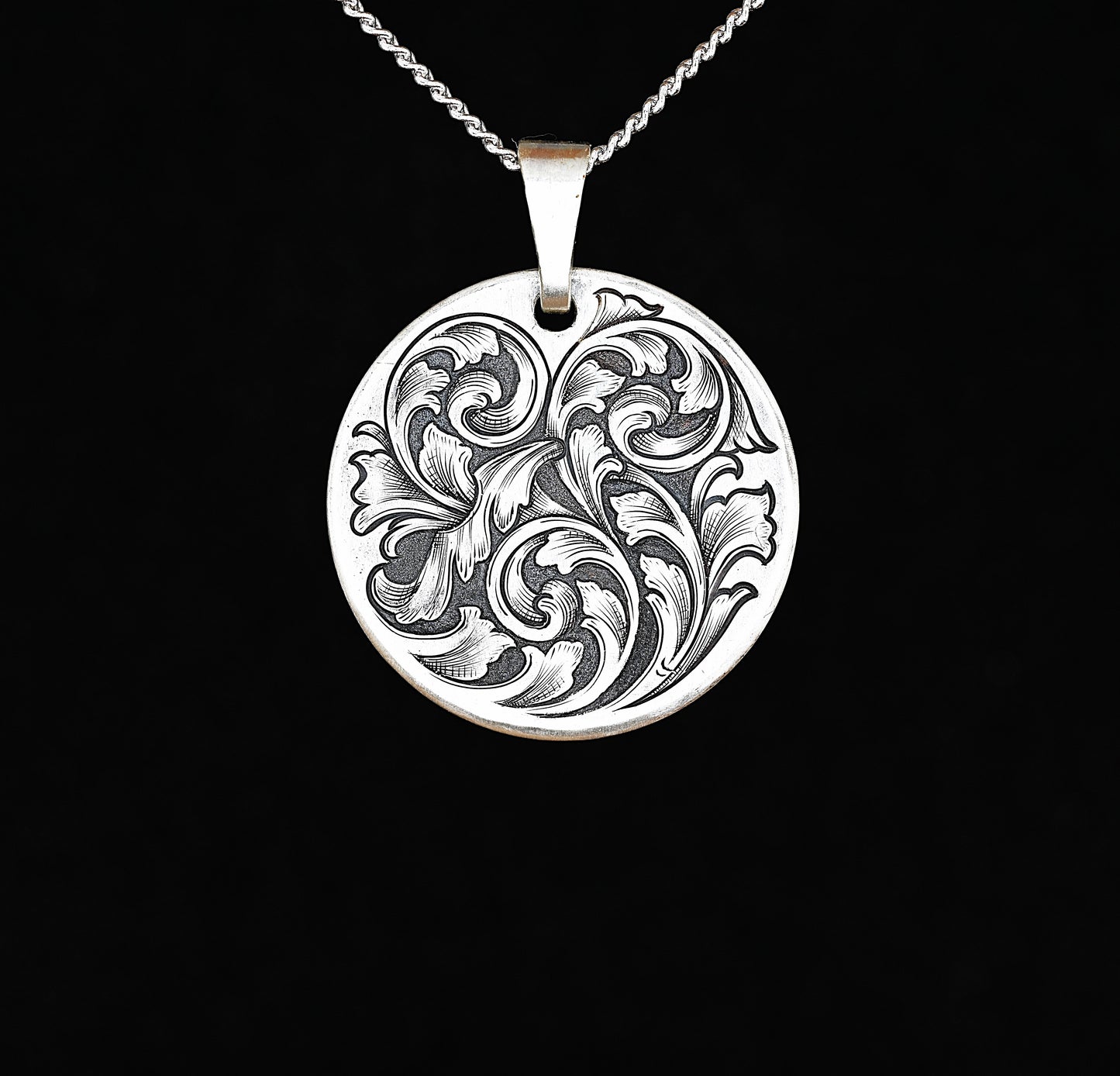 A sterling silver disc pendant with a hand-engraved acanthus vine design