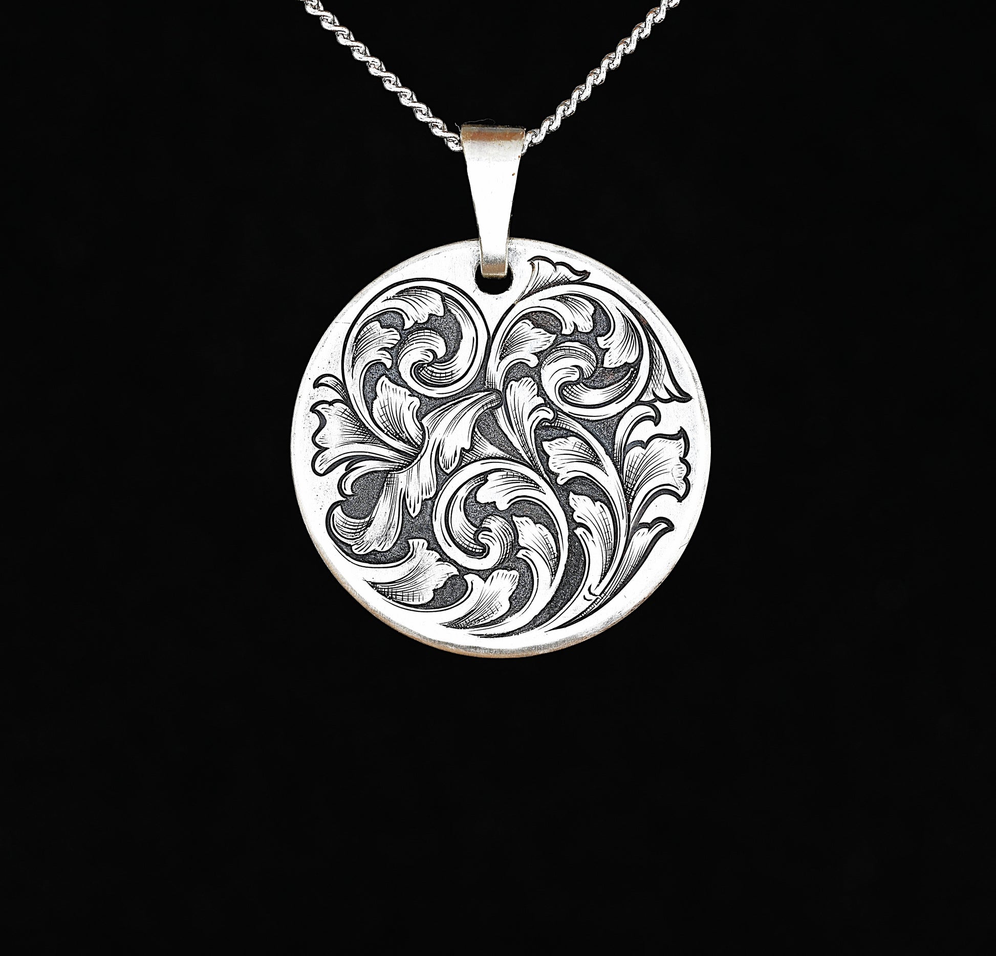 A sterling silver disc pendant with a hand-engraved acanthus vine design