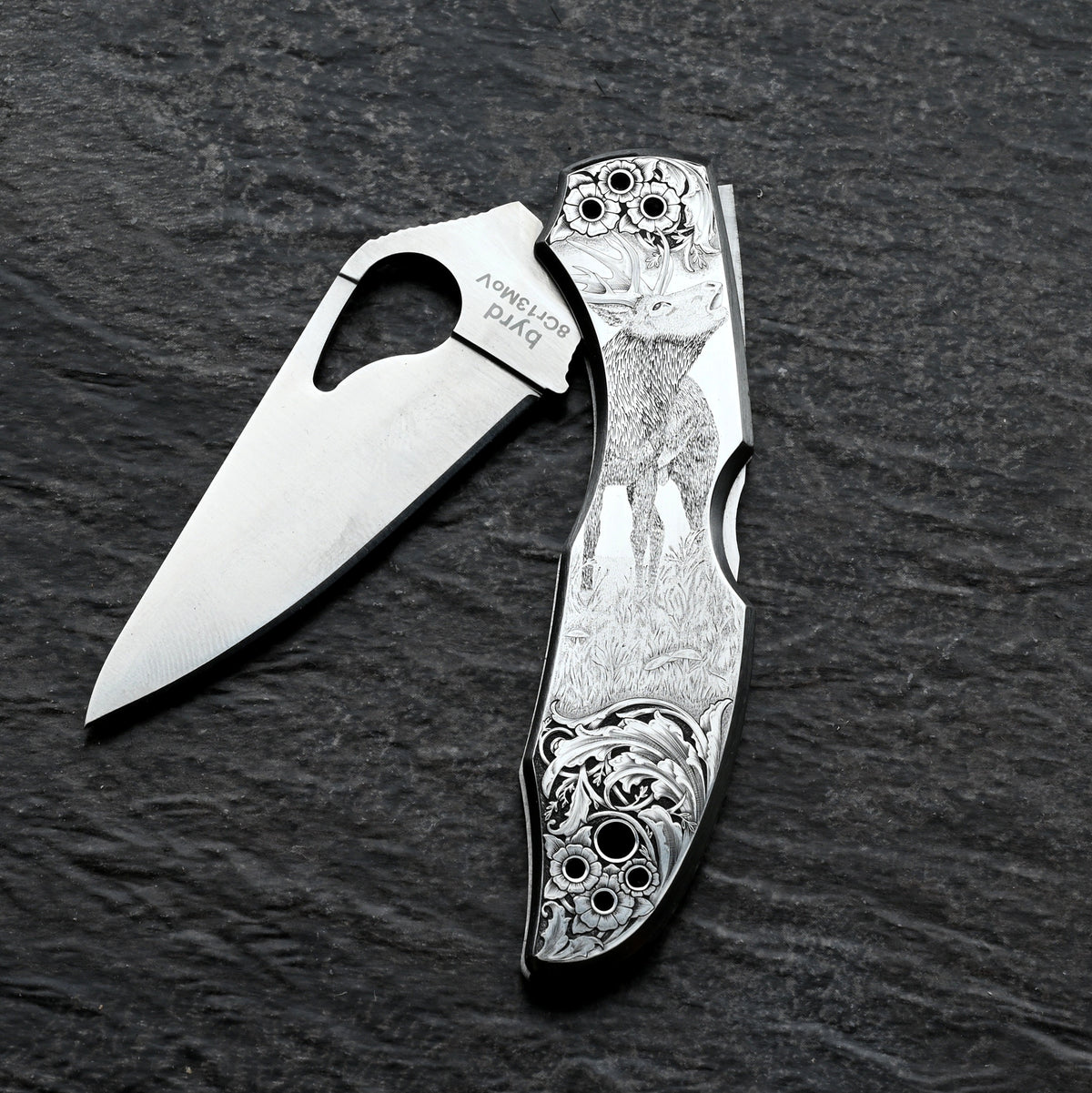 A silver Spyderco knife with an image of a roaring stag and floral embellishments