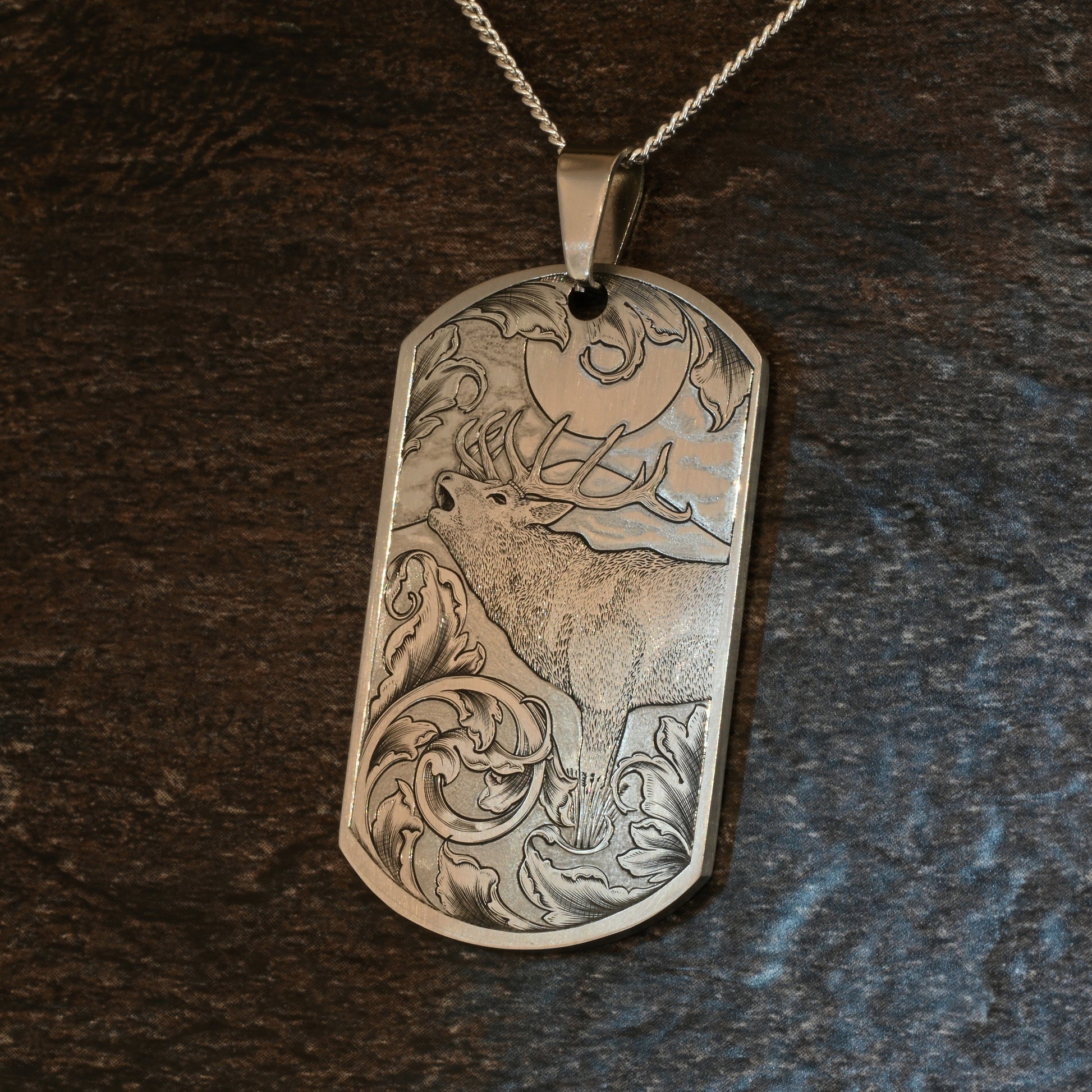 Hand-engraved titanium pendant with red deer calling in the moonlight, surrounded by traditional scrollwork