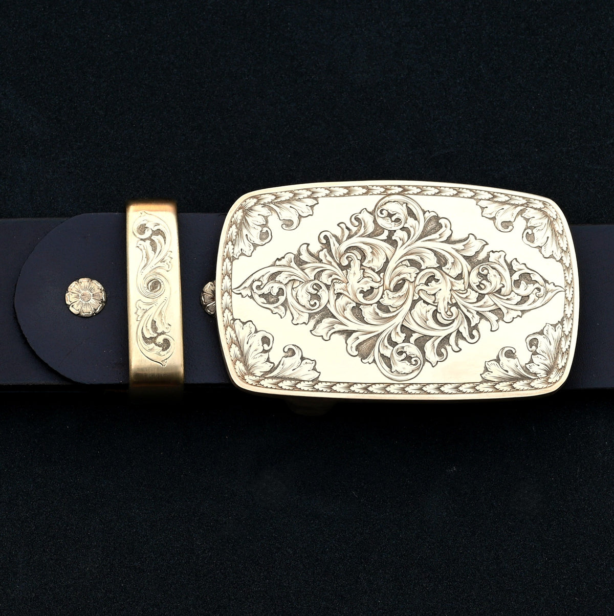 Hand‑engraved brass Western belt buckle set with acanthus scrollwork on dark leather.