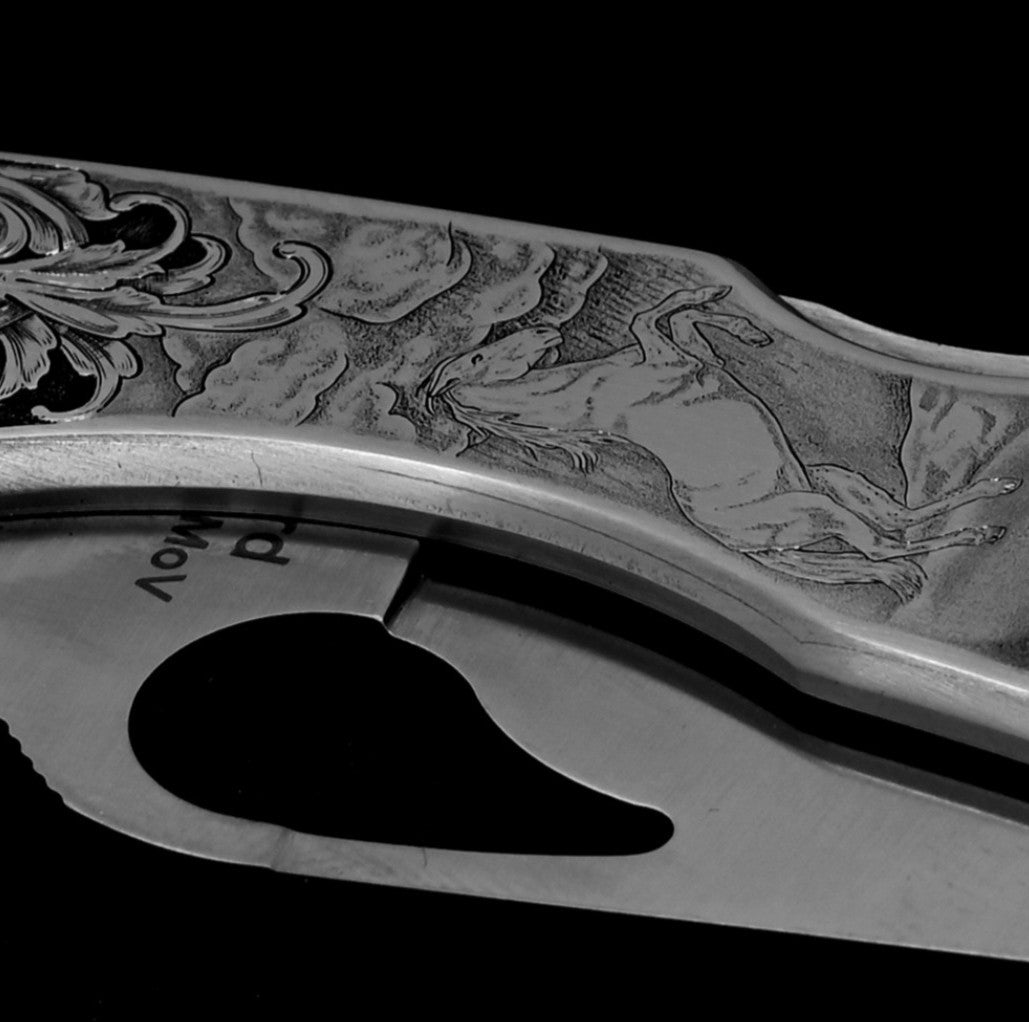 Hand-engraved Spyderco knife in open position with detailed horse scene and relieved acanthus vine.