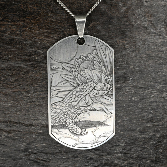 Hand‑engraved titanium pendant featuring a blue‑tongue lizard sunning beside a flower