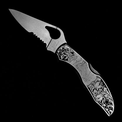 Hand-engraved Spyderco knife in open position with detailed horse scene and relieved acanthus vine.