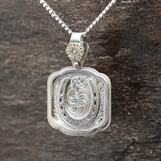 Sterling silver pendant with hand‑engraved horseshoe, scrollwork, and floral details