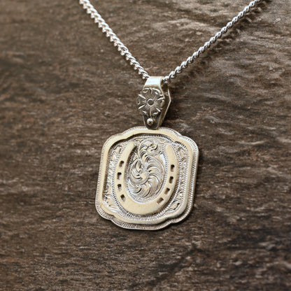 Sterling silver pendant with hand‑engraved horseshoe, scrollwork, and floral details