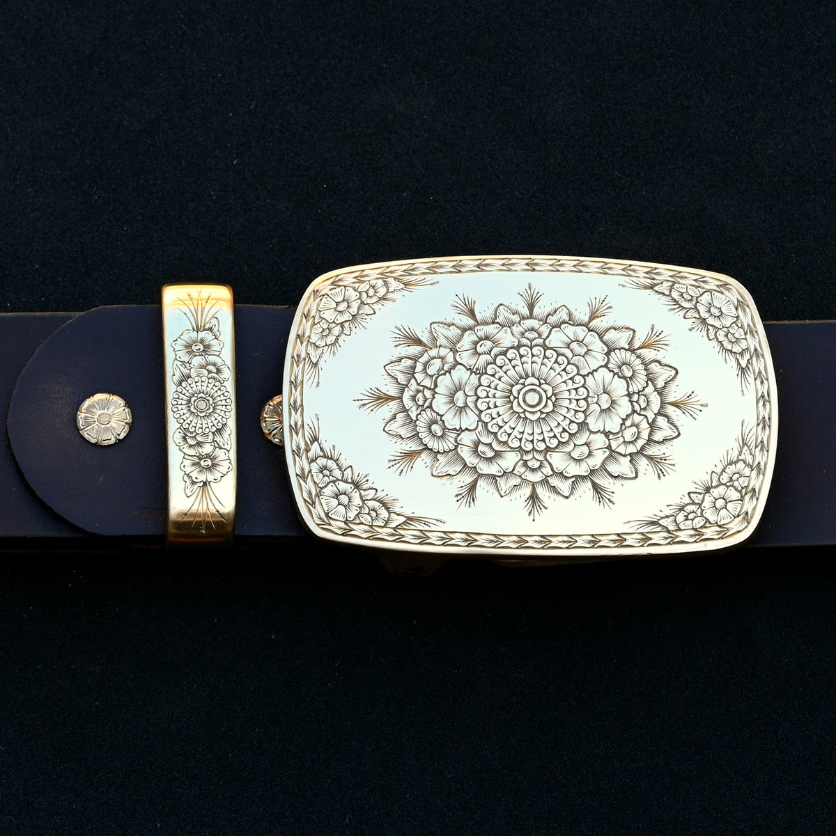 Hand‑engraved brass belt buckle set with floral Western engraving on dark leather.