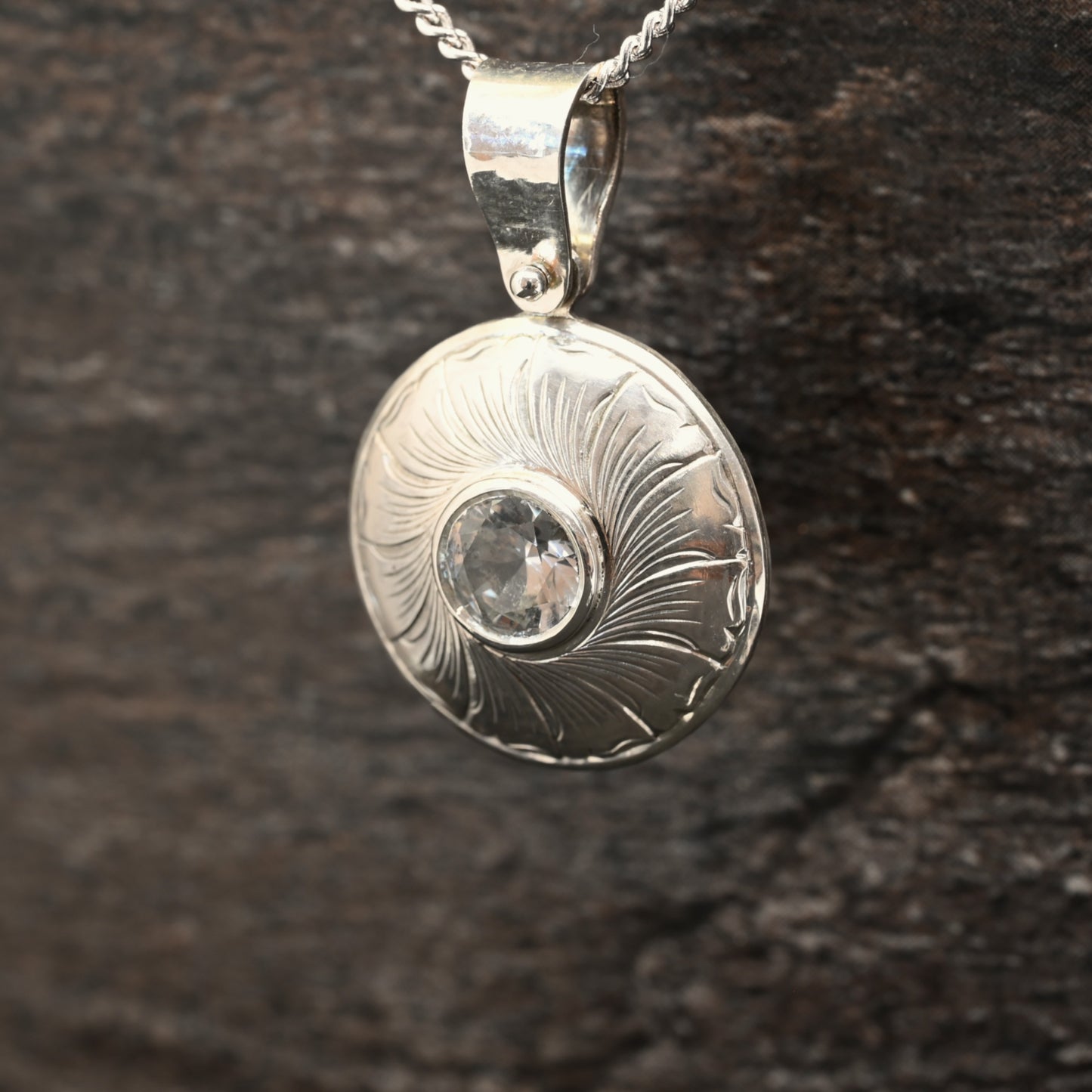 Sterling silver pendant with hand‑engraved leaf motif and white sapphire centre