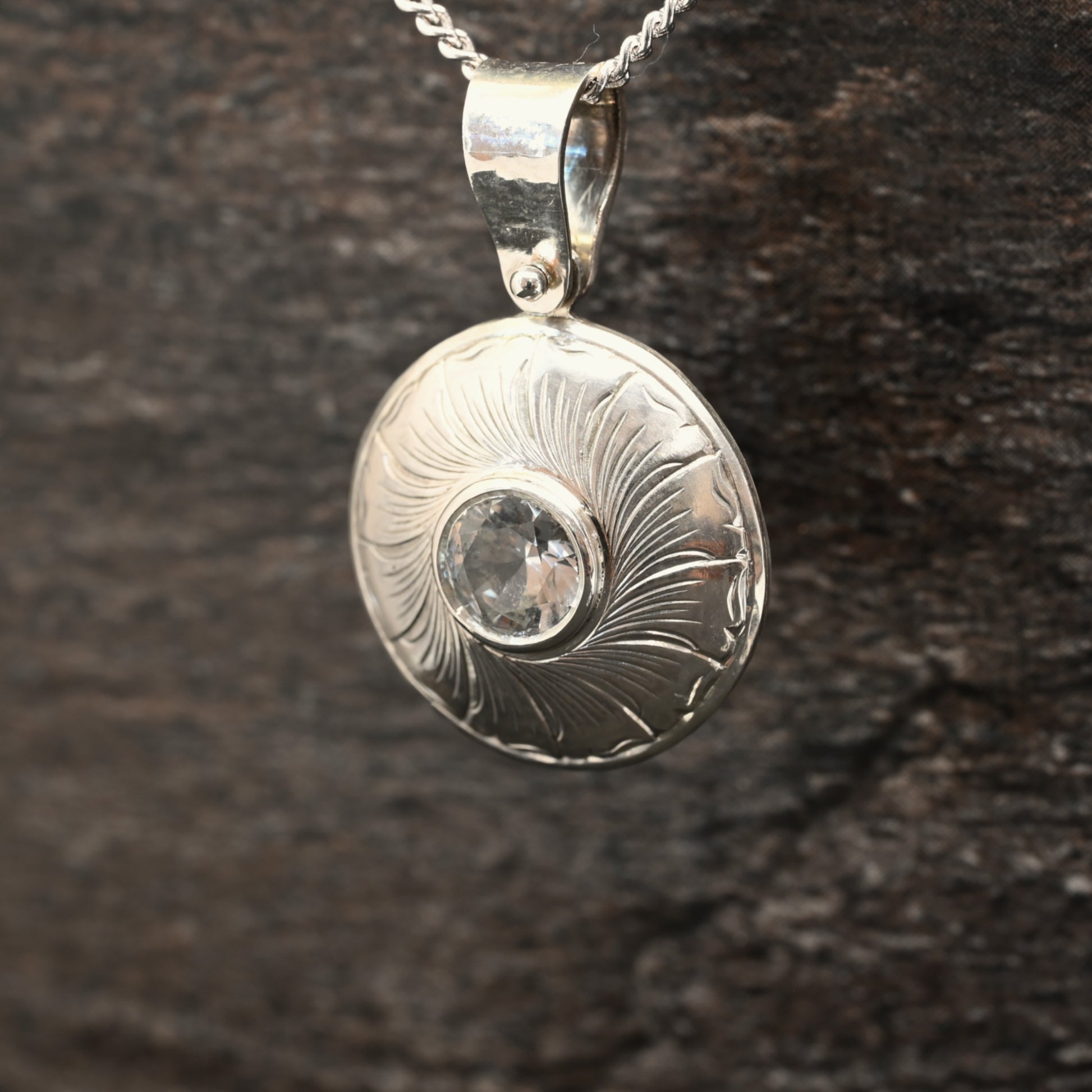 Sterling silver pendant with hand‑engraved leaf motif and white sapphire centre