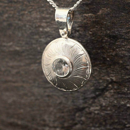 Sterling silver pendant with hand‑engraved leaf motif and white sapphire centre