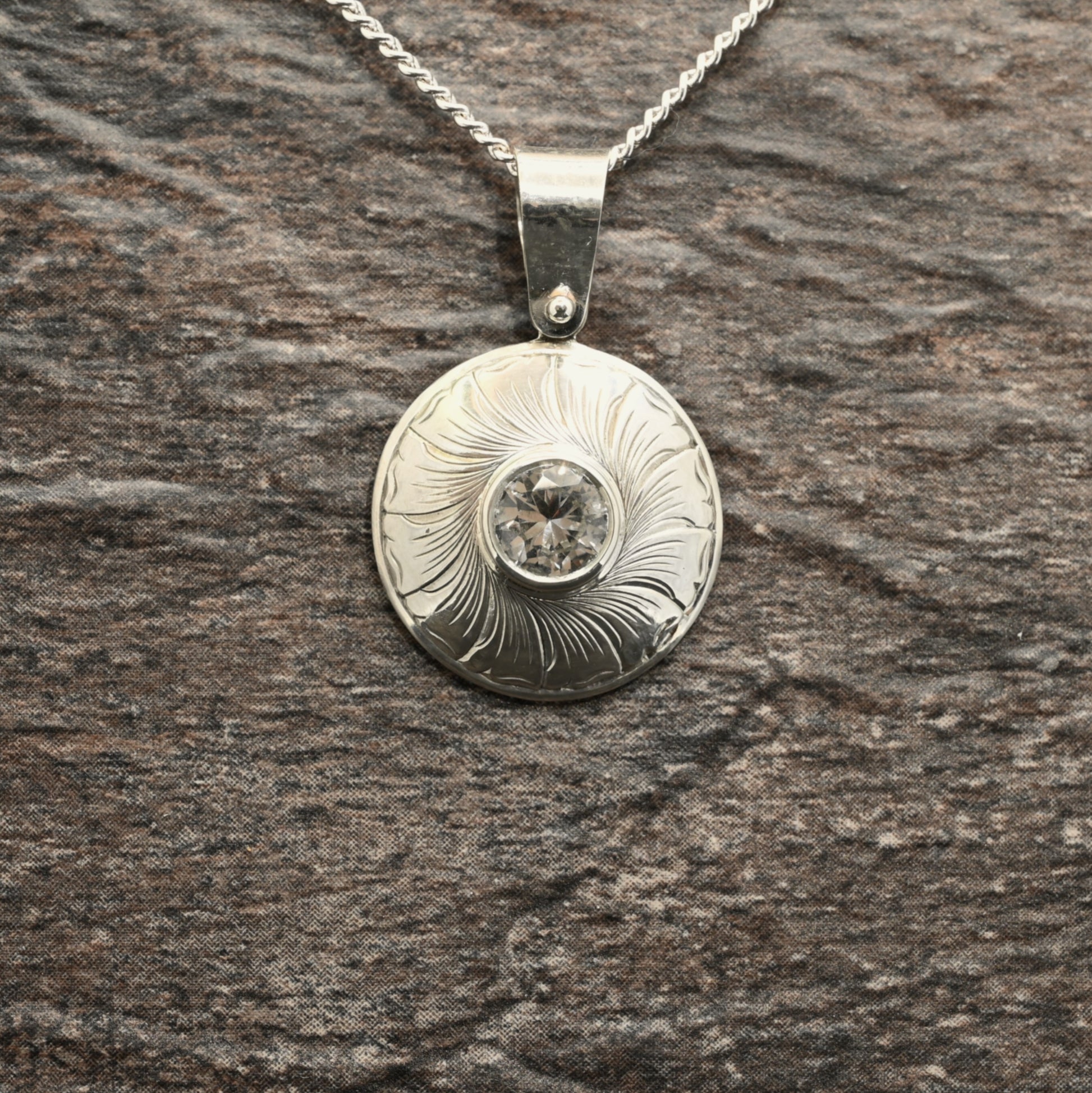 Sterling silver pendant with hand‑engraved leaf motif and white sapphire centre