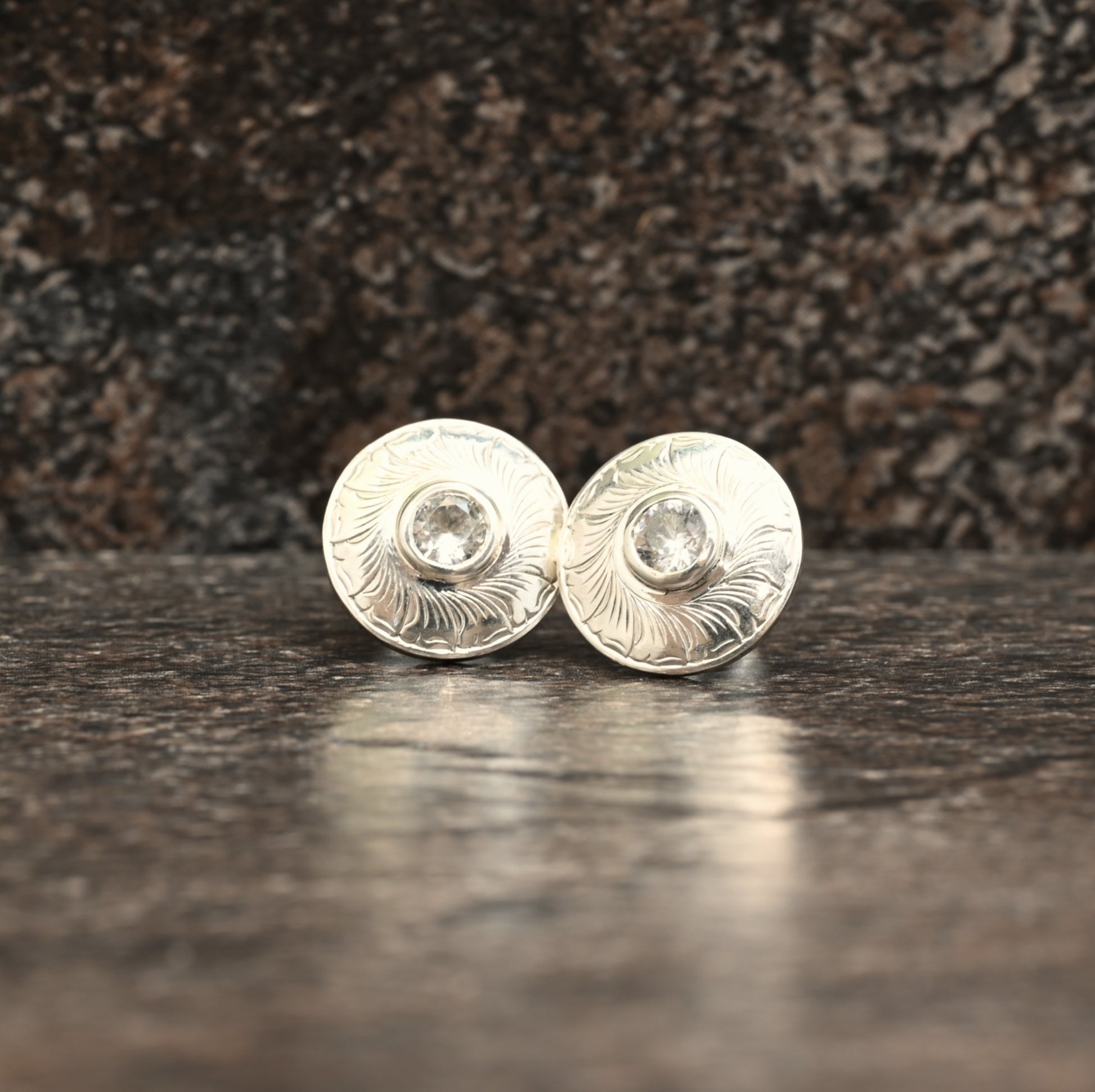 Sterling silver stud earrings with hand‑engraved leaf motif and white sapphire centre